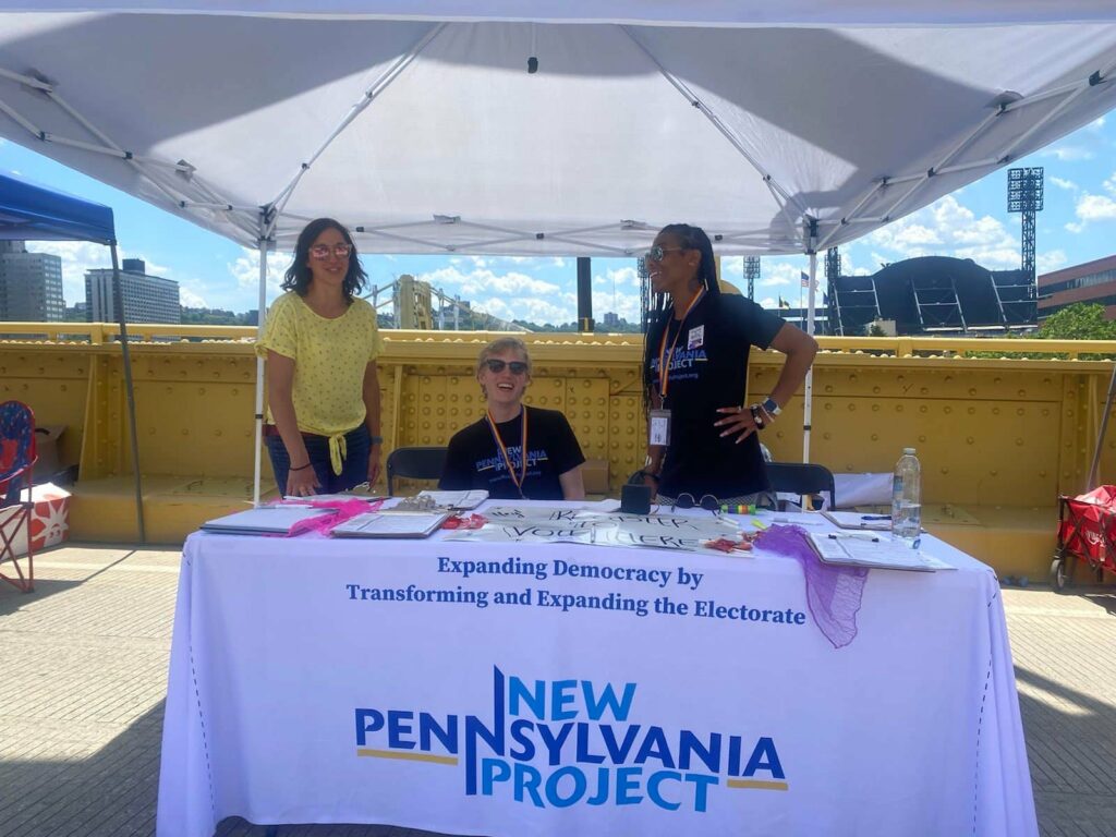 staff seated behind a New Pennsylvania Project table at an outdoor event